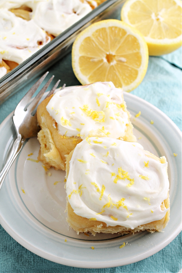 two rolls with icing on saucer These ooey and gooey Lemon Sweet Rolls Recipe has a bright lemony citrus flavor throughout and a delightful gooey lemon cream cheese icing!