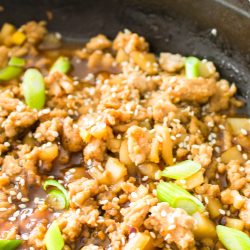 A pan of seasoned ground meat with diced vegetables, topped with sesame seeds and chopped green onions.