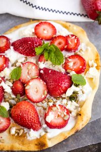 Flatbread topped with whipped cheese, whole and sliced strawberries, crumbled feta, sunflower seeds, and fresh mint leaves.